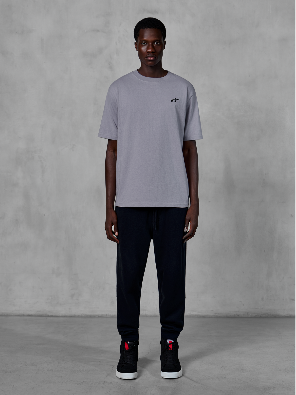 Alpinestars Essentials Ageless SS Tee, Short Sleeve T-Shirt, Silver, featuring a small black logo on the chest, styled with black joggers and sneakers, casual motorsport streetwear