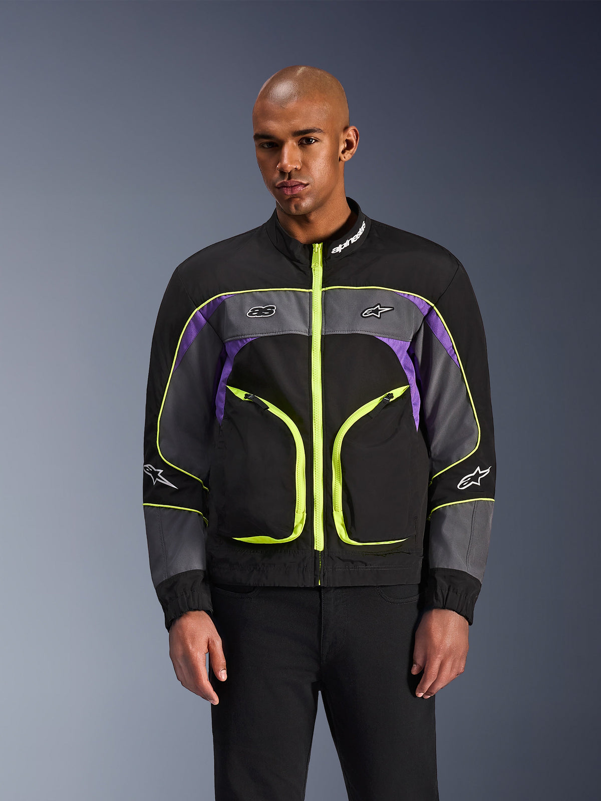 Alpinestars Unite Jacket, urban motorcycle jacket, Black Asphalt and Violet with neon yellow accents, featuring large front pockets with neon zippers, high collar with white branding, worn by model, contemporary streetwear-inspired protective gear