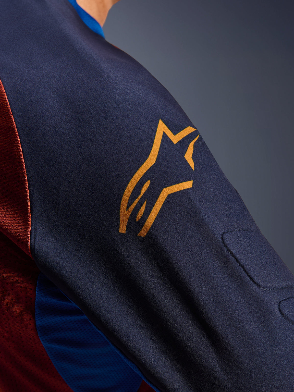 Alpinestars Maxdura Dual Jersey, close-up of the Mood Indigo sleeve with a yellow Alpinestars logo, showing integrated spacer mesh padding and Rust Brown mesh torso fabric, technical adventure motorcycle apparel