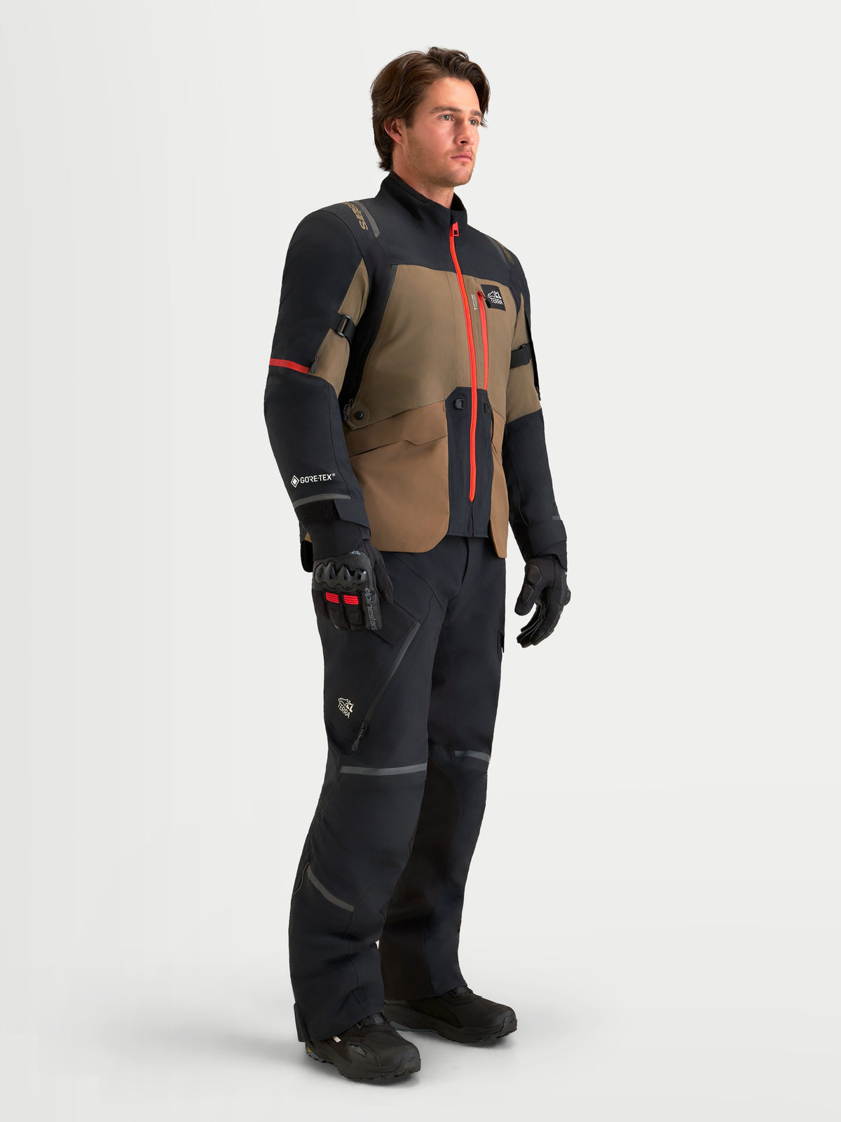 Alpinestars St-7 V2 2L Gore-Tex Gear Set, adventure touring motorcycle jacket and pants in black and olive brown, worn by a model showing waterproof textile construction and high-visibility red zipper details.