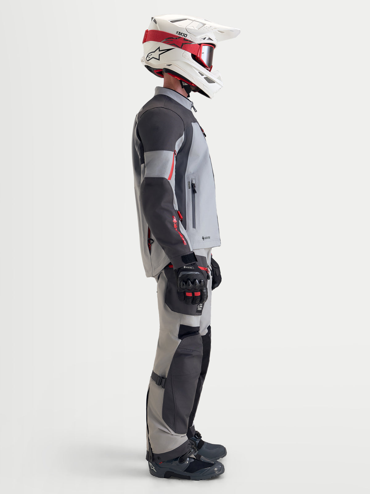 Alpinestars Arenis Gore-Tex Gear Set, men's adventure touring motorcycle jacket and pants in gray and black, side profile view on a model wearing matching gear and helmet, waterproof all-terrain riding apparel.
