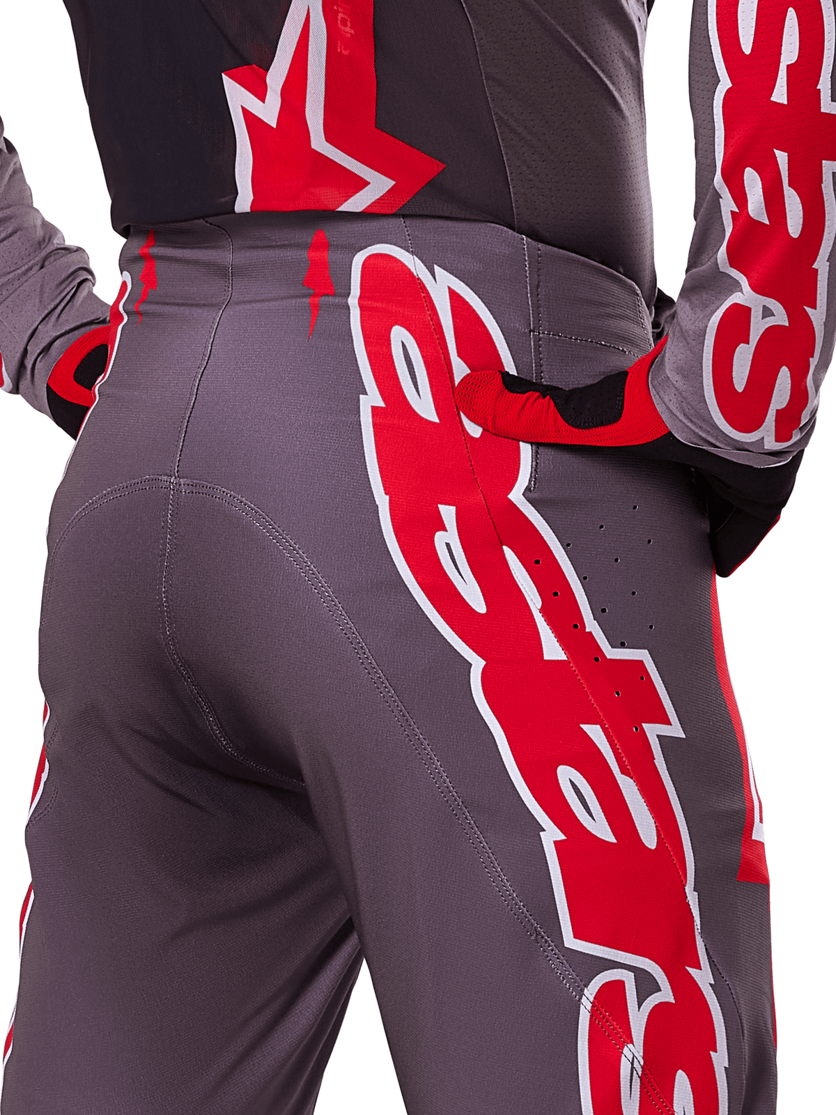 Alpinestars 2025 Supertech Lipan Pants, Motocross Pants, Smoke Bright Red, rear close-up view showing dark gray fabric with bold red graphics, worn with matching red and black gloves and jersey, featuring ventilation perforations and ergonomic stitching for off-road performance