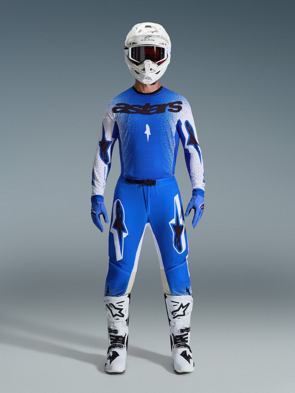 Motocross rider wearing complete racing gear, blue and white jersey with black astars branding, 2026 Supertech Scenz Pants in Ucla Blue White with bold star logos, white helmet, blue gloves, and white boots, coordinated athletic racing outfit