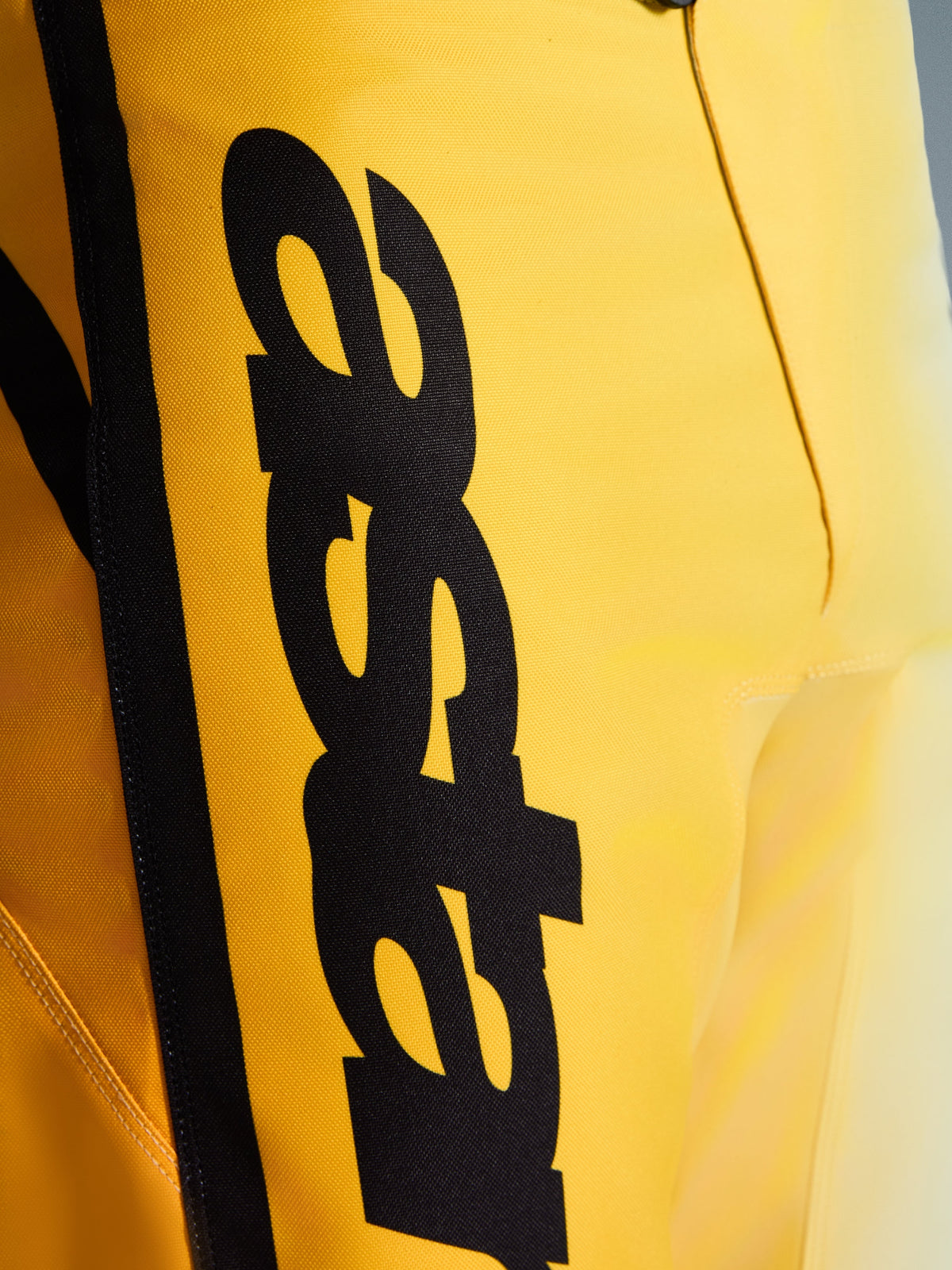 Close-up of Alpinestars 2026 Fluid Apex Pants, Motocross Pants, Yellow and Black, featuring a large vertical black logo, textured durable material, and ergonomic details for off-road performance