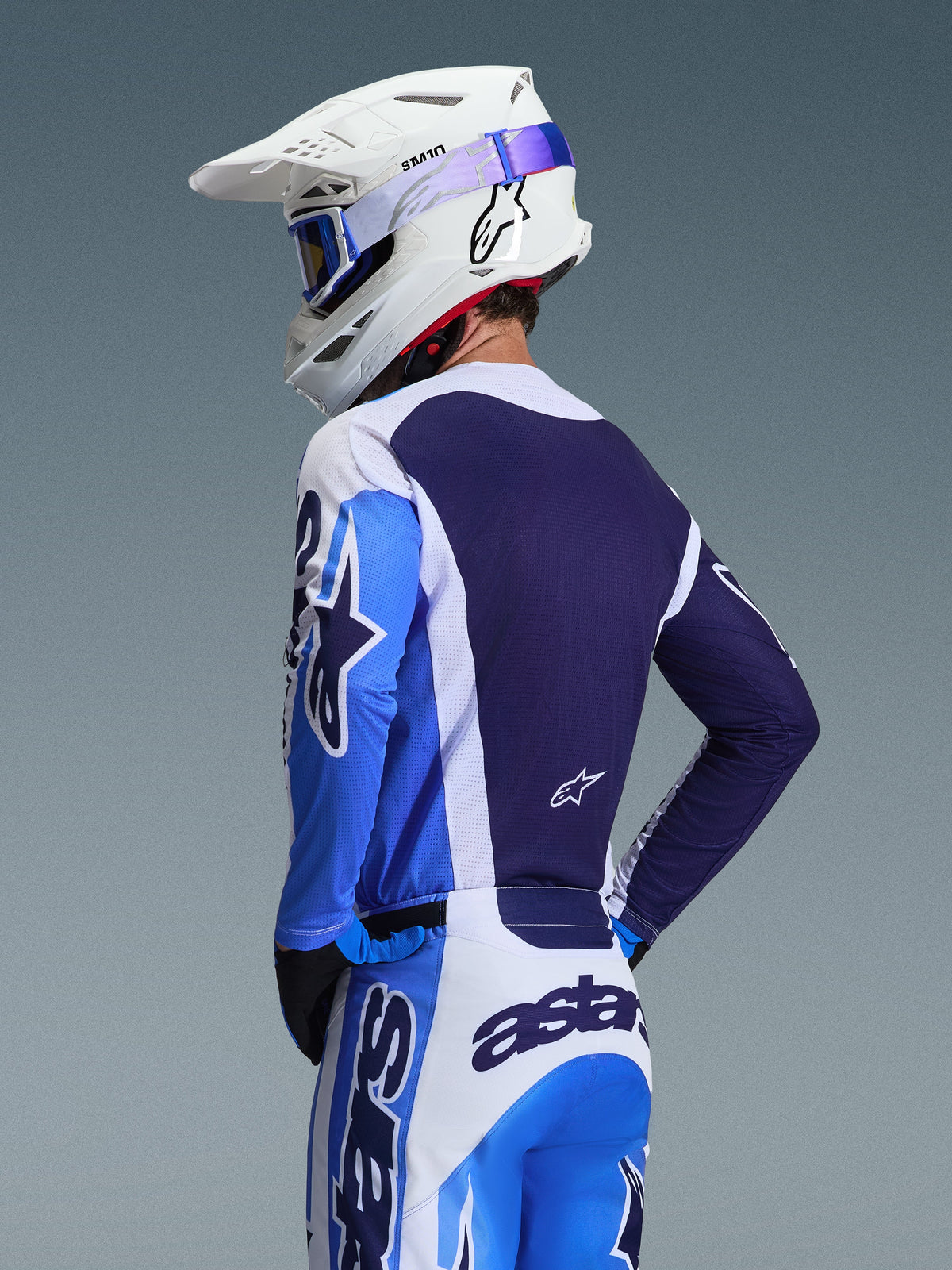 Motocross rider wearing the Alpinestars 2026 Racer Air Portl Jersey in Ucla Blue and White, rear view highlighting the breathable navy blue mesh back panel, worn with matching pants and a white Alpinestars helmet with blue goggles, coordinated motocross gear set.