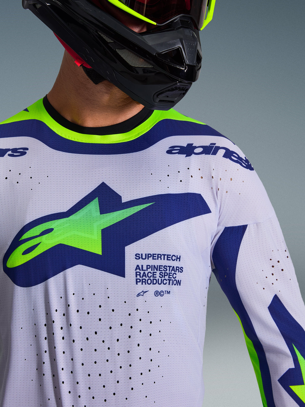 Alpinestars 2026 Supertech Vista Jersey, Motocross Jersey, Light Gray with Yellow Fluo and Blue accents, worn by rider with black helmet and neon yellow goggles, features large green and blue Astars logo, laser-cut ventilation holes, and athletic race fit design
