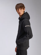 Alpinestars Frontal Hoodie, black pullover fleece, model wearing with side profile view, white alpinestars wordmark on sleeve, kangaroo pocket, casual motorsport-inspired streetwear