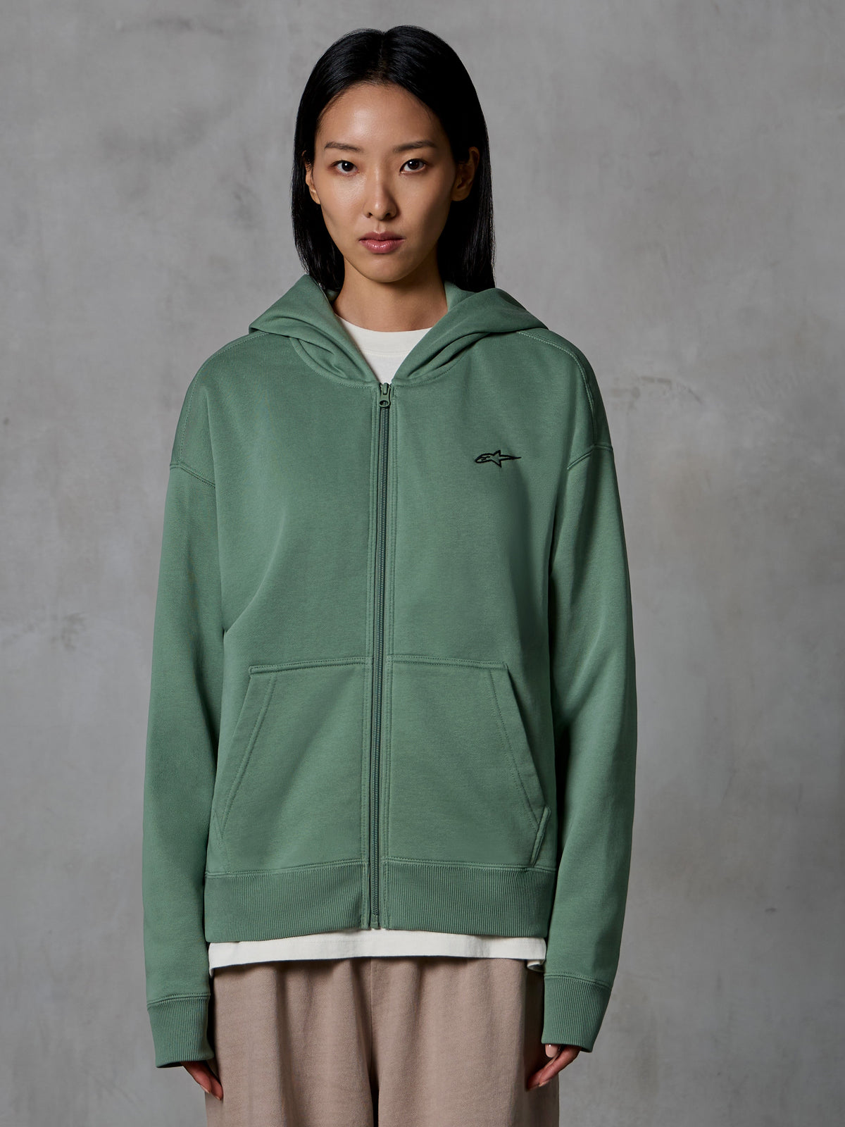 Alpinestars Essentials Ageless Zip Hoodie, Cactus Green, casual streetwear worn by female model, zip-up fleece sweatshirt with small black logo on the chest, front pockets, relaxed fit for everyday wear