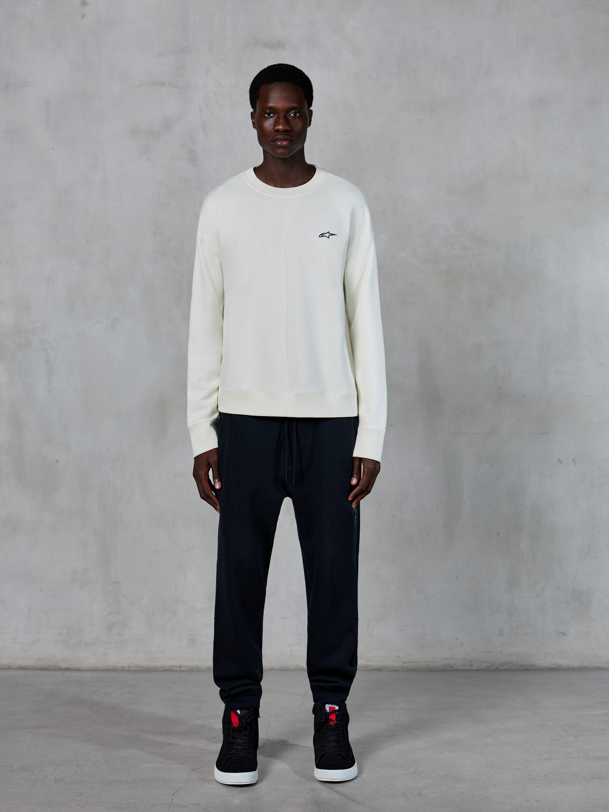 Alpinestars Essentials Ageless Crew, crewneck sweatshirt, Off White with small black star logo, worn by model with black joggers, casual motorsport-inspired streetwear