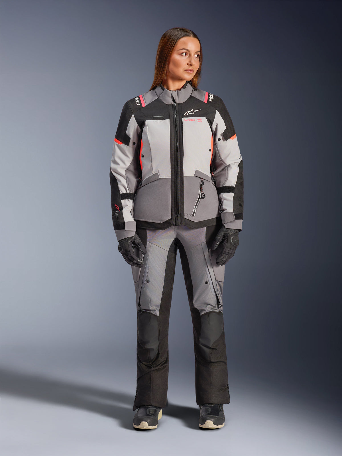 Alpinestars Stella Andes V4 Drystar® Jacket and Pants, women's adventure textile gear set in dark gray, ice gray, black, and coral fluo, front view on a model wearing the complete waterproof riding suit.