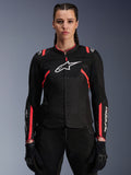 Alpinestars Woman Stella T-Sps Air V2 Jacket, Black and Diva Pink, textile motorcycle jacket featuring breathable mesh panels and pink accents, white Alpinestars logo on chest, worn by a female model with black riding pants and gloves.