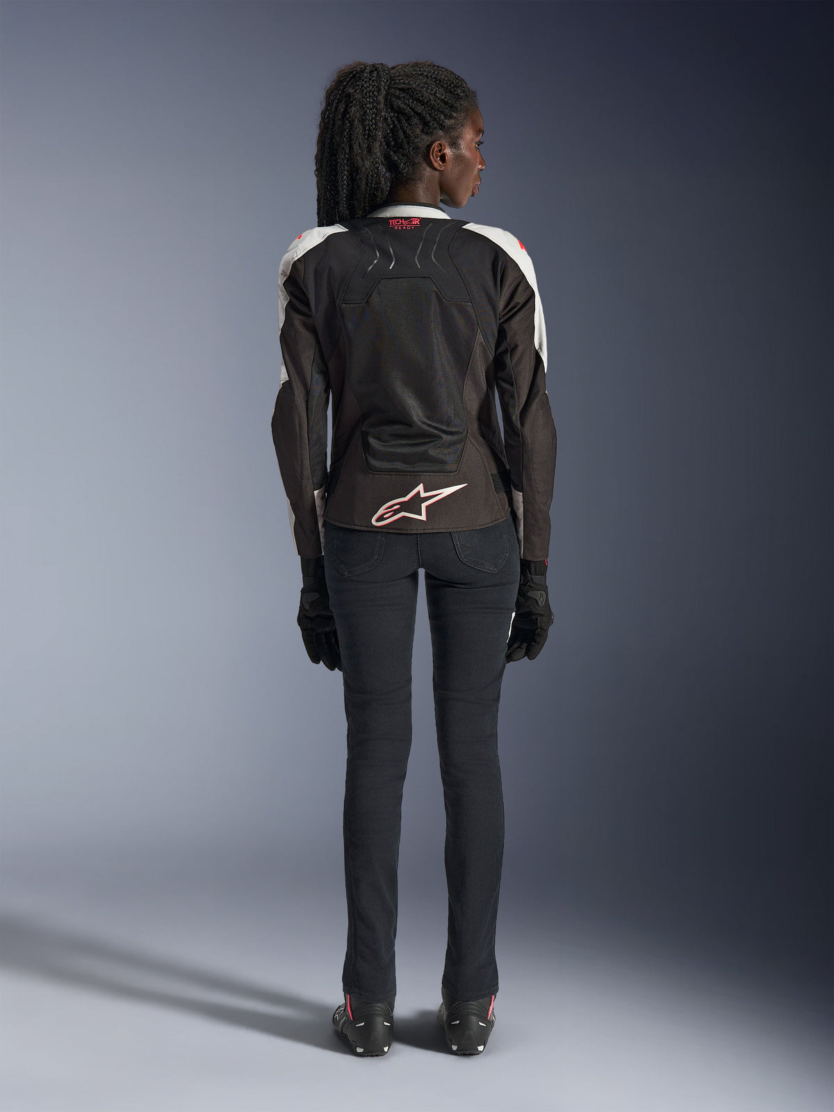 Alpinestars Woman Stella SMX Air Jacket, Ice Gray Black Coral Fluo, back view showing ventilated mesh panels, white Alpinestars logo on the lower back, and Tech-Air Ready branding at the collar, worn with black motorcycling pants and gloves.