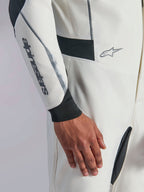 Alpinestars Hypertech V3 Suit, close-up of white auto racing suit featuring black and silver accents, Alpinestars logo on the forearm, black knitted wrist cuff, and dark stretch panels for mobility, professional motorsport apparel.