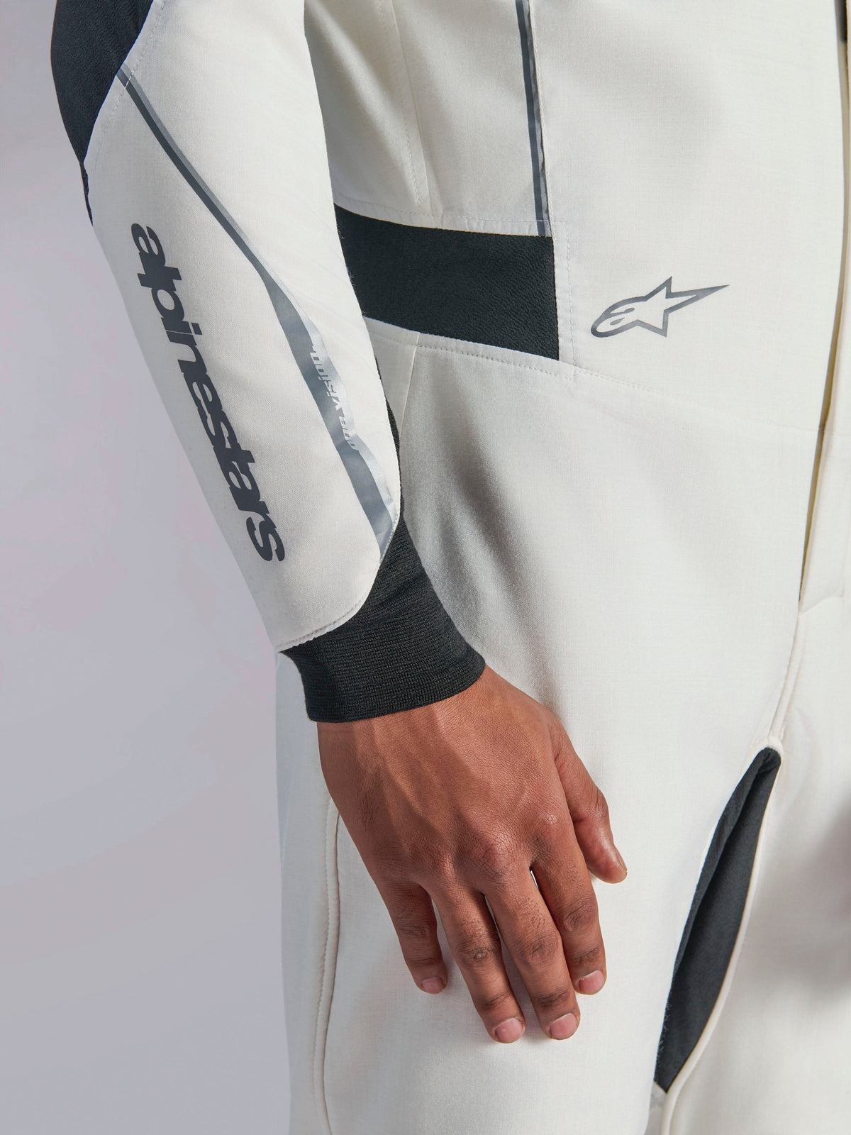 Alpinestars Hypertech V3 Suit, close-up of white auto racing suit featuring black and silver accents, Alpinestars logo on the forearm, black knitted wrist cuff, and dark stretch panels for mobility, professional motorsport apparel.