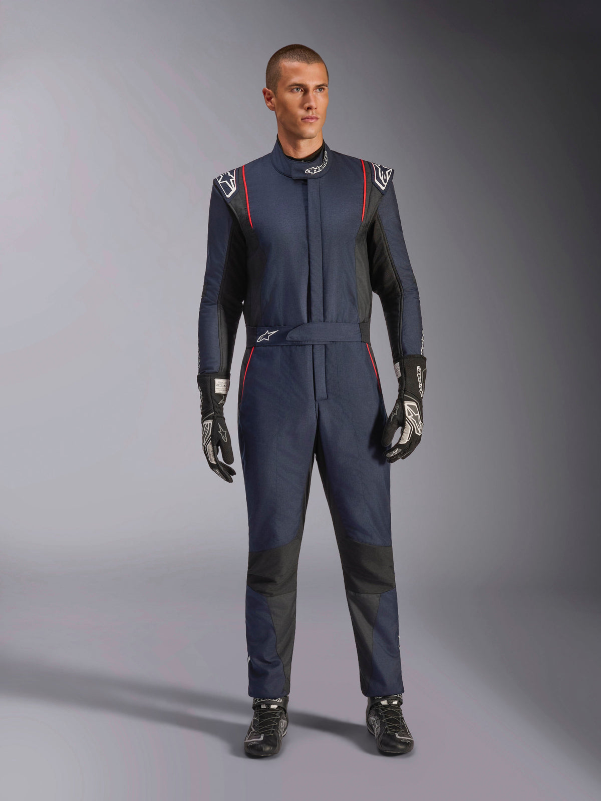 Alpinestars GP Tech V4 Suit, professional auto racing suit in Blue Navy and Black with Red piping, one-piece FIA certified racing gear, worn with black racing gloves and footwear, motorsport driver apparel