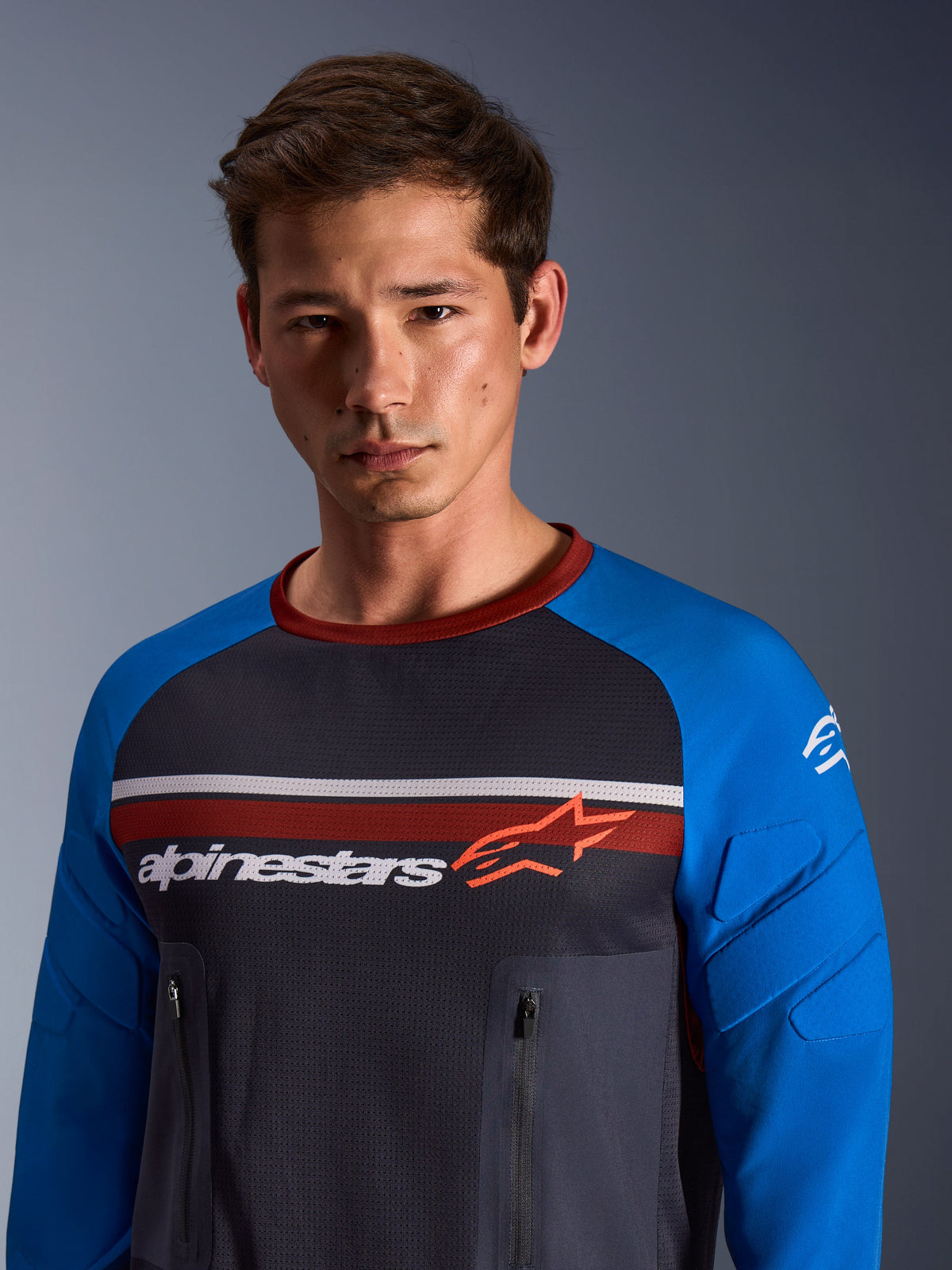 Alpinestars Maxdura Dual Jersey, Deep Gray and Royal Blue, worn by a male model, featuring a mesh torso, royal blue sleeves with integrated padding, and vertical zippered chest pockets with Alpinestars branding across the chest.