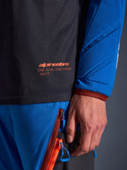 Close-up of Alpinestars Maxdura Dual Jersey in Deep Gray and Royal Blue, featuring an orange logo and 'One Goal One Vision' text on the mesh torso, padded sleeve with reinforced geometric panels, technical adventure riding gear detail