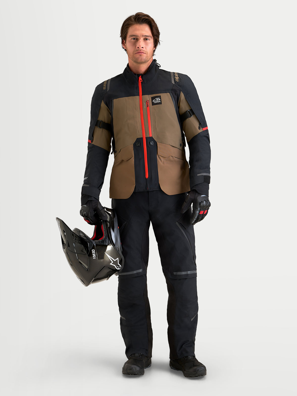 Alpinestars St-7 V2 2L Gore-Tex® Gear Set, men's adventure touring motorcycle jacket and pants in black and khaki with a bright red front zipper, worn by a model holding a black helmet.