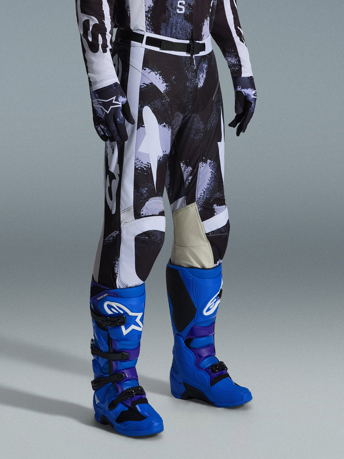 Alpinestars 2026 Racer Lahnd Pants, Motocross Pants, Iron Camo gray and black pattern, worn with bright blue racing boots and matching gloves, featuring white panels and goat leather inner knees, performance-driven off-road gear