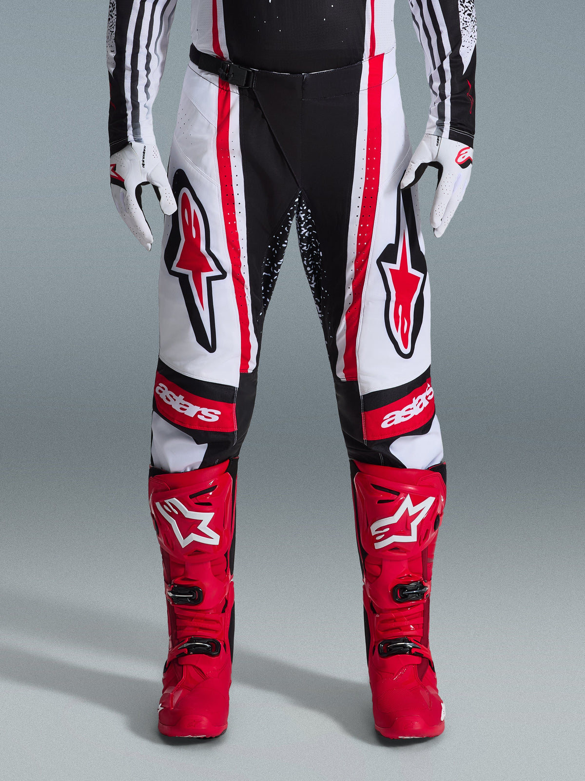 Alpinestars 2026 Techstar Nomur Pants, Motocross Pants, Black White and Red, worn with matching red boots and white gloves, featuring bold red logos on the thighs and 'astars' branding on the knees, multi-panel racing design for off-road performance