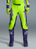 Alpinestars 2026 Supertech Vista Pants, Motocross Pants, Fluorescent Yellow Purple and Black, worn with matching gloves and purple boots, featuring large gradient logos on thighs, perforated zones for ventilation, and a professional athletic design for off-road racing