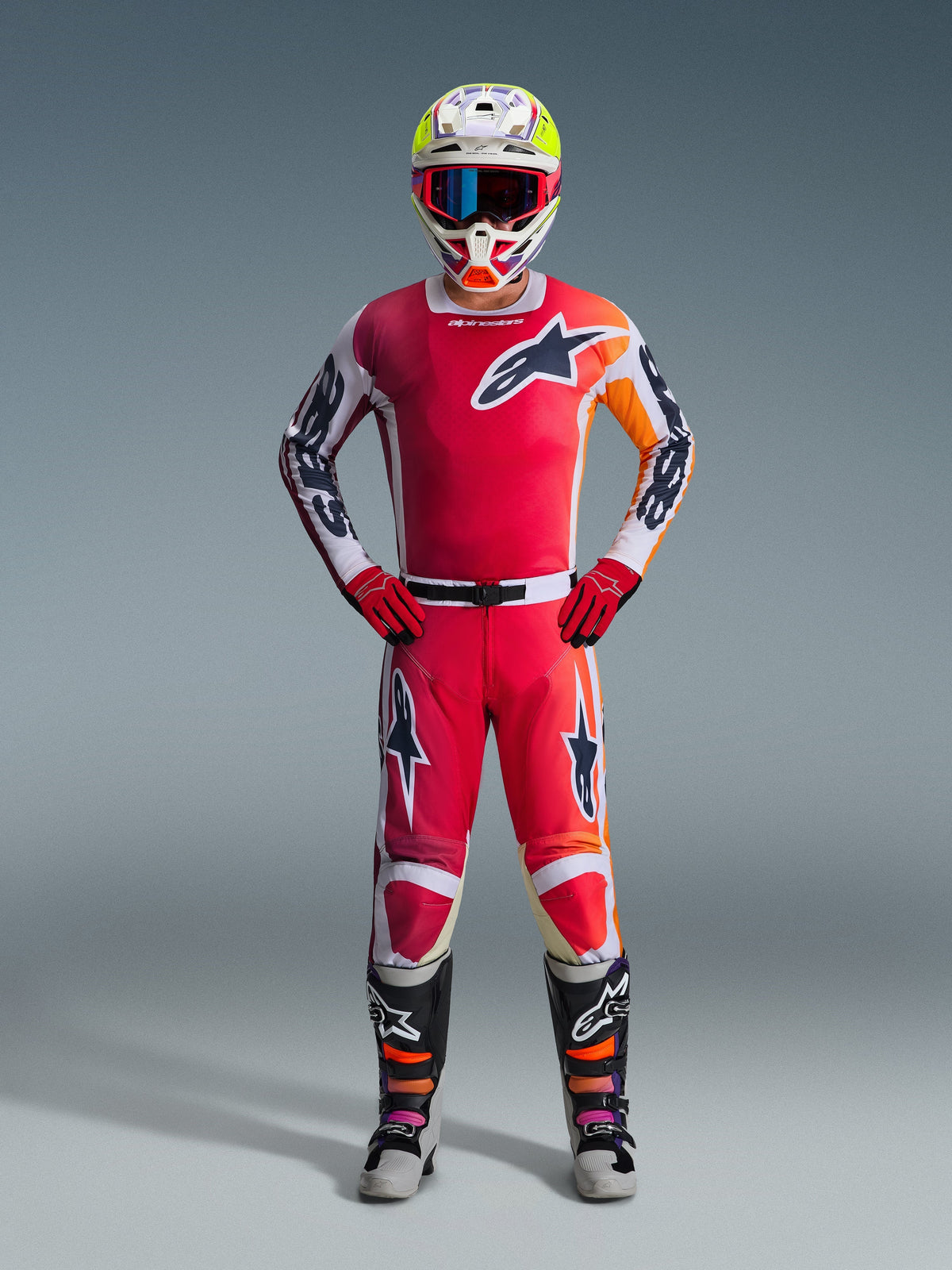 Motocross rider wearing the Alpinestars 2026 Racer Portl Jersey in Red, featuring white and orange graphic accents, paired with matching motocross pants, red gloves, a colorful racing helmet with goggles, and black and white technical boots, complete off-road racing gear set