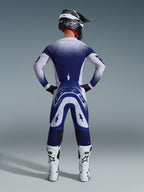 Motocross rider from behind wearing the Alpinestars 2026 Supertech Scenz Jersey, Light Gray and Dark Blue with a stippled gradient design, matching motocross pants, white racing boots, and black helmet, complete off-road racing outfit.