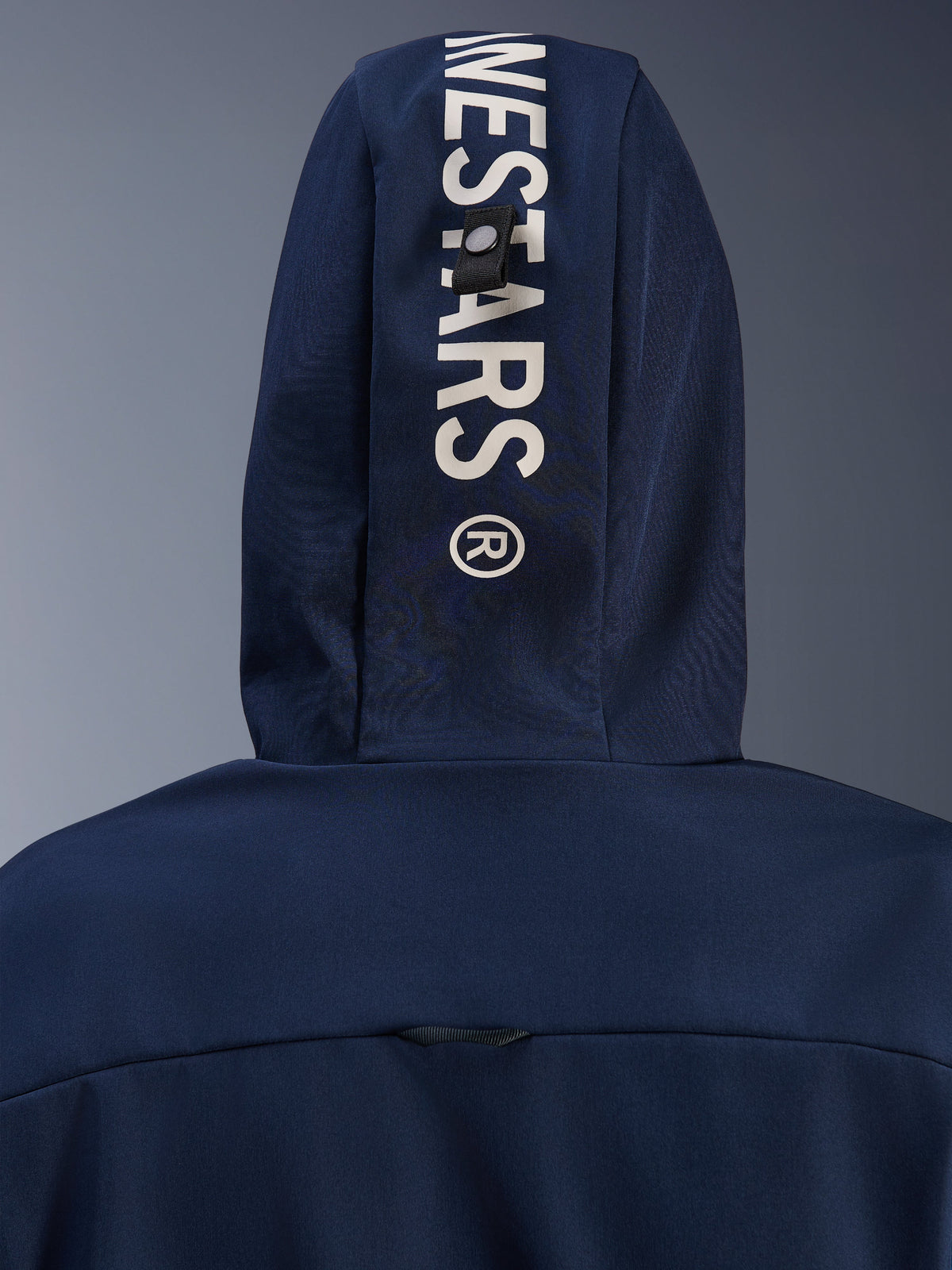Alpinestars Radium Tech Hoodie in Night Navy Royal Blue, close-up of the back hood featuring vertical white Alpinestars branding and a secure loop attachment system, urban motorcycle technical apparel.