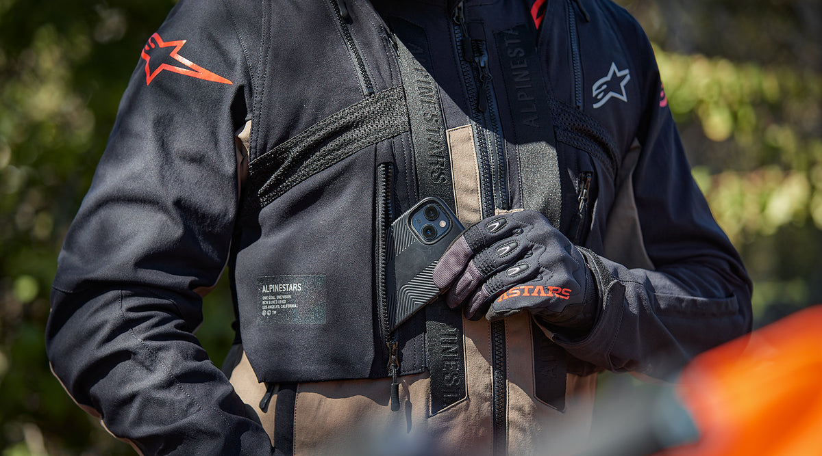 Alpinestars Techdura Jacket and tactical vest, Black and Falcon Brown, rider storing a phone in a zippered chest pocket.