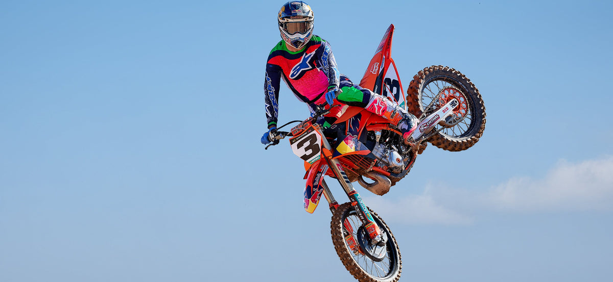 Alpinestars Limited Edition Supertech Records Gear Set and S-M10 Helmet, multicolor motocross outfit mid-jump.