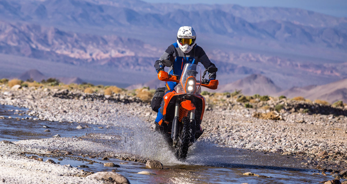 Alpinestars Maxdura Drystar XF Jacket in Blue and Gray, waterproof adventure gear on a rider crossing a desert stream.