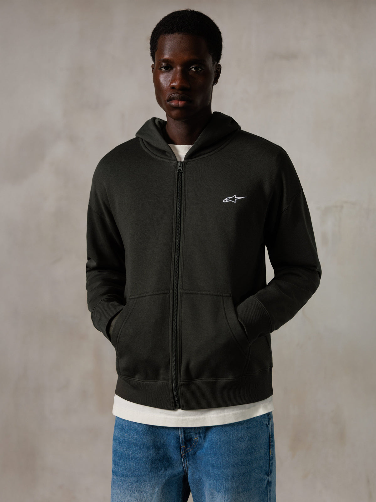 Alpinestars Essentials Ageless Zip Hoodie, Off Black, full-zip hoodie with a small white Alpinestars logo on the chest, relaxed fit, worn by a model with blue jeans and a white t-shirt, casual motorsport-inspired streetwear