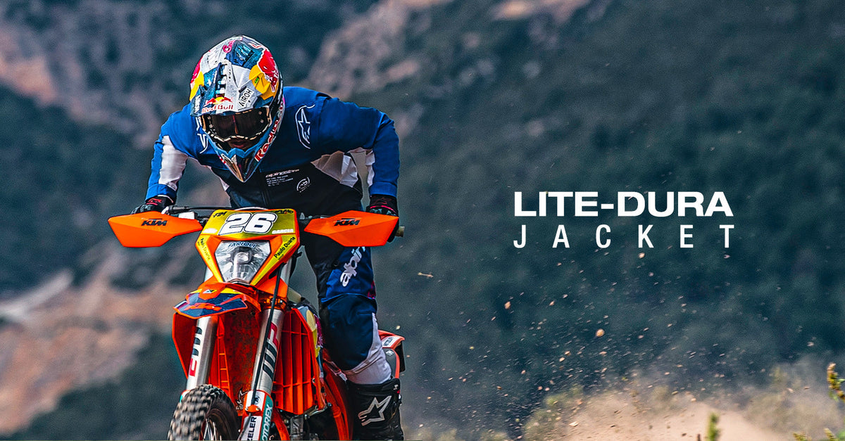 Alpinestars Lite-Dura Softshell Jacket in navy and white, worn by a rider on an orange motorcycle in an off-road setting.