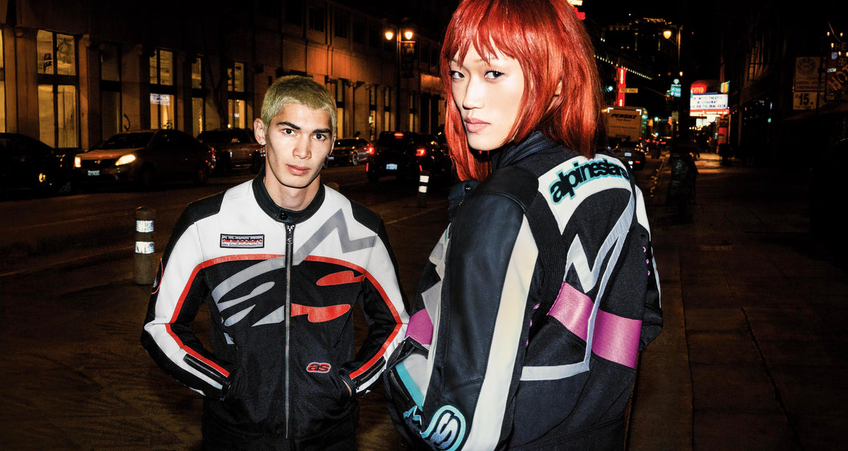 Alpinestars Idles Jackets in black and off-white, vintage urban motorcycle racing style worn on a city street at night.