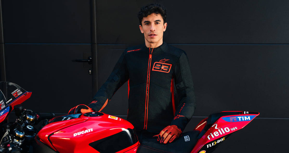 Alpinestars MM93 C-1 Air Jacket and gloves, urban motorcycle riding gear, black and red, worn by Marc Márquez with a Ducati racing bike.