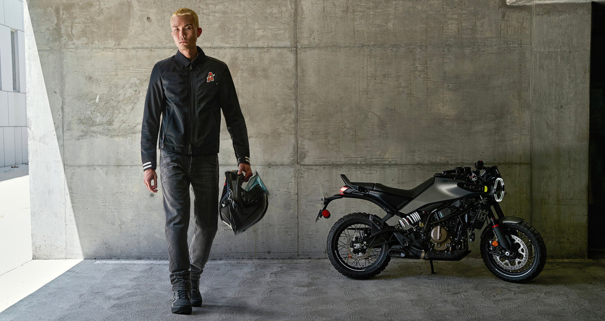 Alpinestars Ignite Air Jacket, gray and black urban motorcycle jacket, shown with a rider carrying a helmet by a motorcycle.