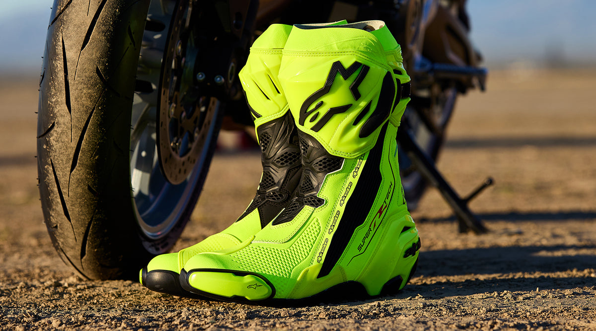 Alpinestars Supertech R Boots in fluorescent yellow and black, racing motorcycle boots displayed by a sportbike tire.