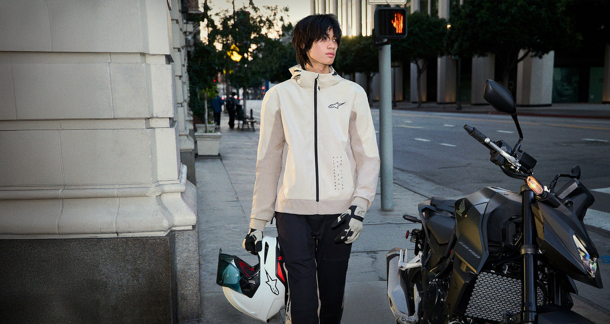 Alpinestars Radium Tech Hoodie in Mastic Aluminum is a windproof urban motorcycle jacket shown on-model in a city setting.