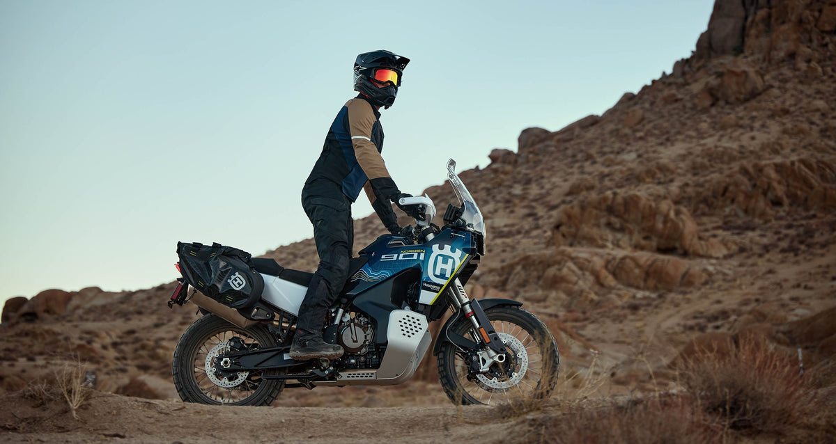 Alpinestars ST-2 Air Jacket, adventure touring motorcycle jacket in tan and navy, shown on a rider in a desert landscape.