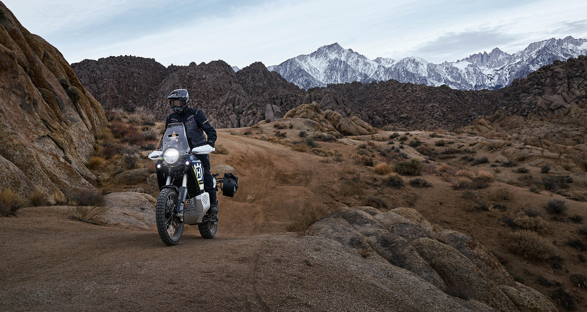 Alpinestars ST-7 2L GORE-TEX Jacket in black and dark gray, worn by an adventure rider in a rugged mountain landscape.