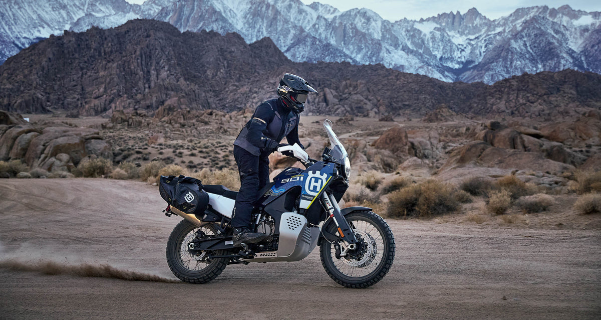Alpinestars ST-7 2L GORE-TEX adventure jacket in black and dark gray, worn by a rider in a desert mountain landscape.