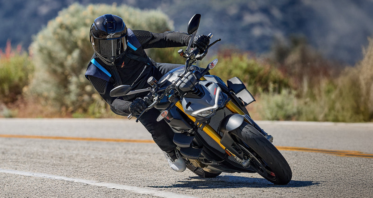 Alpinestars T-Stunt Air Jacket, men's black and blue textile sport jacket, worn by a rider leaning into a curve on a road.