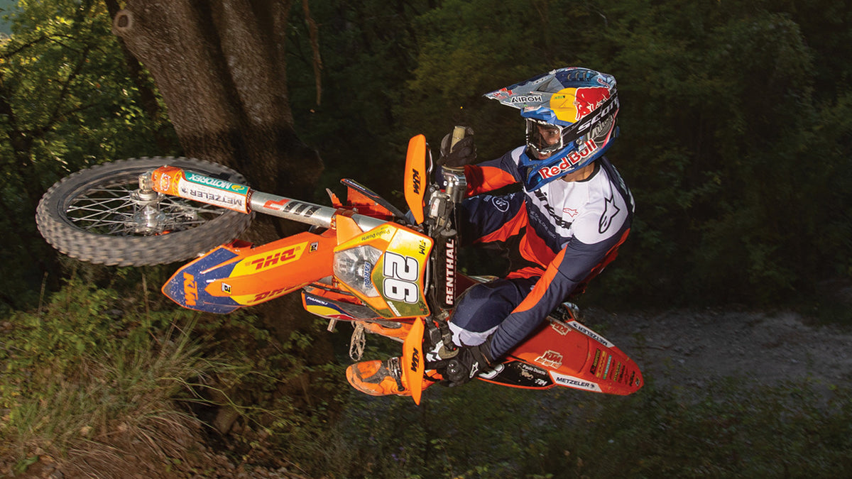 Alpinestars Pro-Dura Jersey AND Pro-Dura Pants, navy and orange enduro gear worn by a rider jumping an off-road bike.