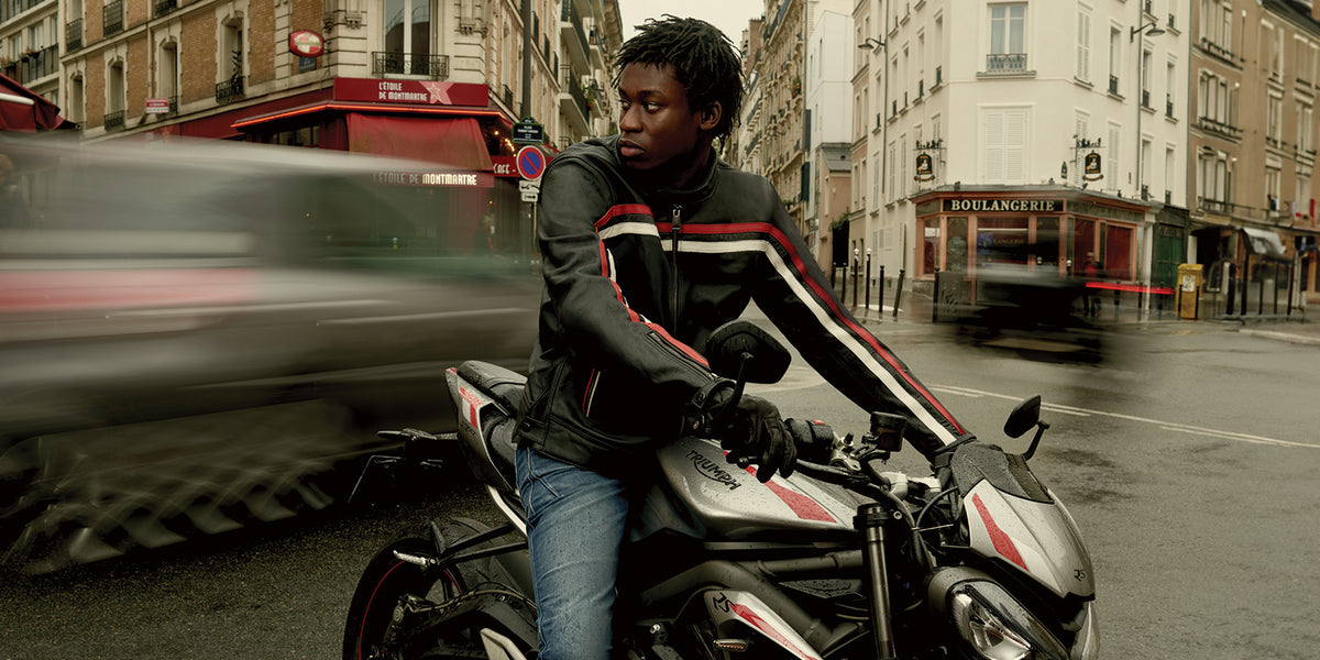 Alpinestars Dyno Leather Jacket in black with red and ecru stripes, worn by a man on a motorcycle in an urban street.