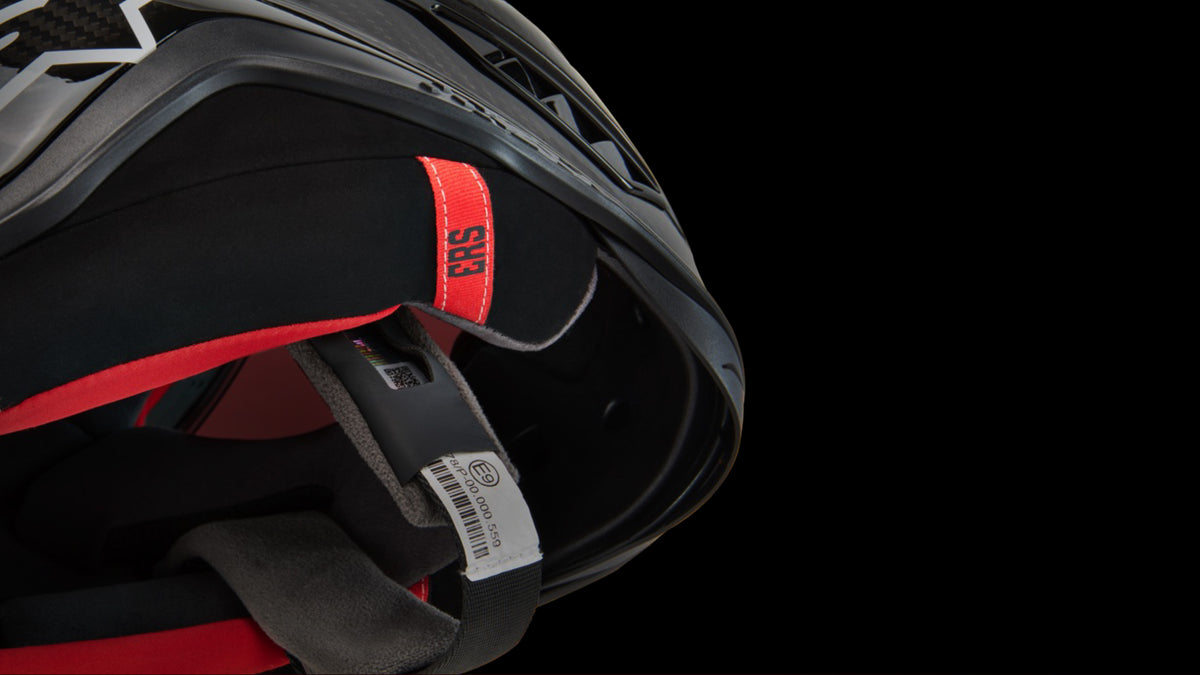 Alpinestars motorcycle helmet detail featuring red ERS Emergency Release System tab and ECE safety certification label.